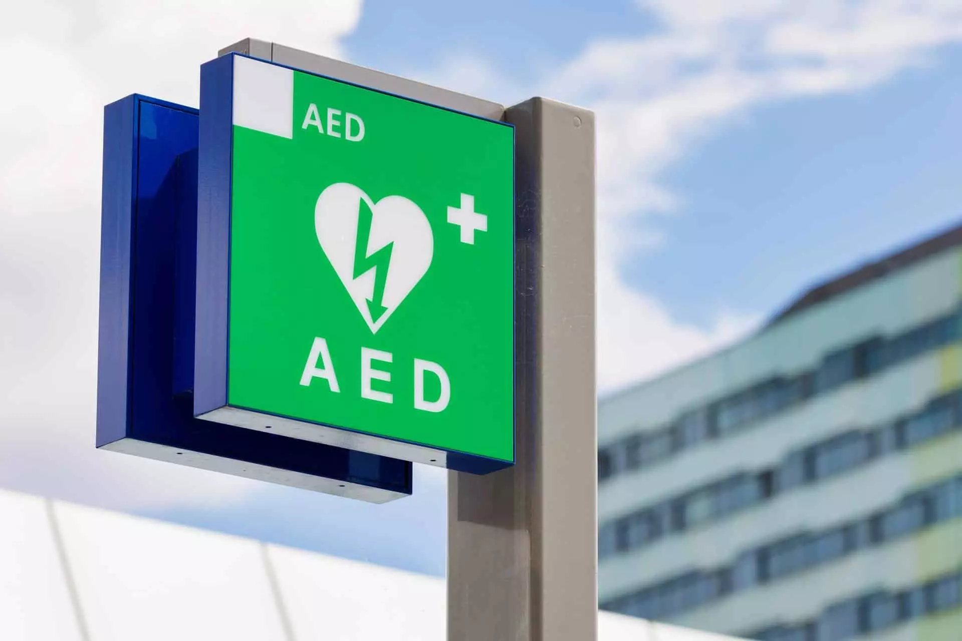 Panneau de signalisation AED vert fixé sur mât devant un immeuble, indiquant un défibrillateur