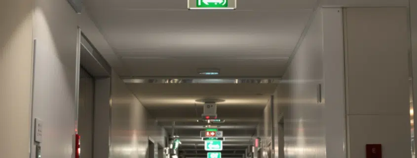 Couloir de bureau avec panneaux de signalisation incendie lumineux indiquant les issues de secours