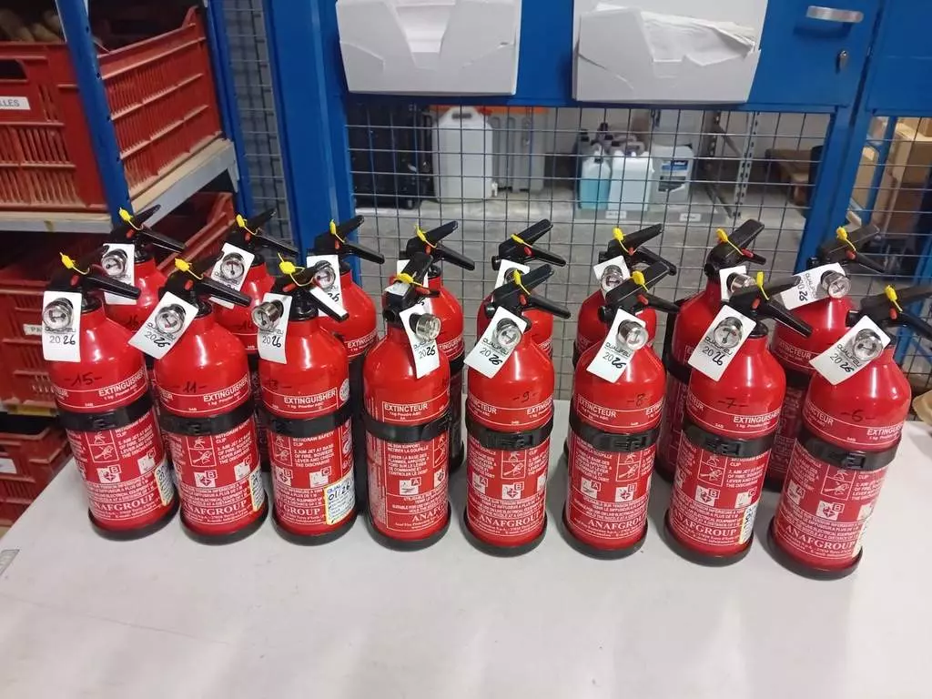 Rangée d'extincteurs Qualifeu rouges à poudre alignés sur un établi en atelier