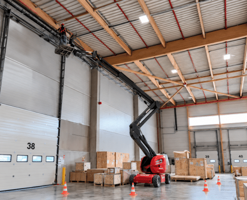 Technicien en nacelle élévatrice installant un système de sécurité incendie dans un entrepôt industriel