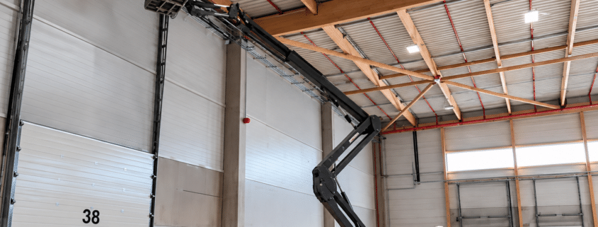 Technicien en nacelle élévatrice installant un système de sécurité incendie dans un entrepôt industriel