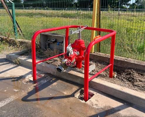 Poteau incendie rouge protégé par un arceau de sécurité derrière une clôture grillagée