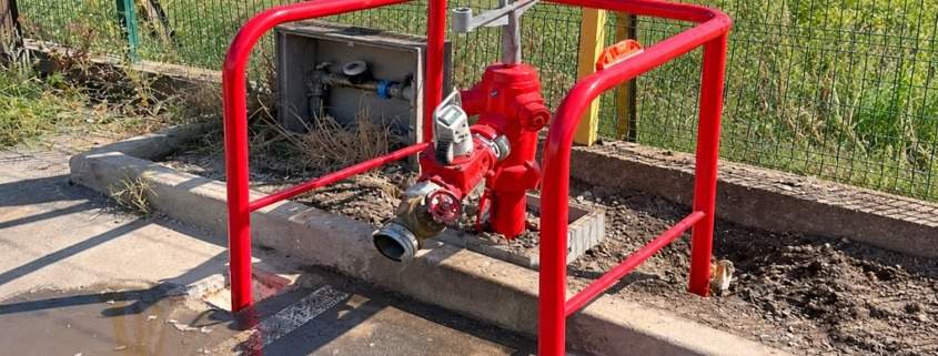 Poteau incendie rouge protégé par un arceau de sécurité derrière une clôture grillagée