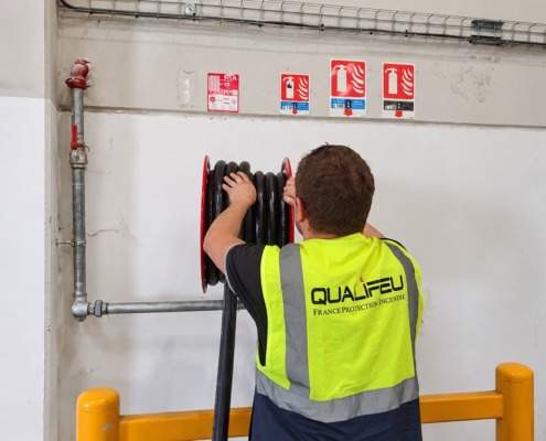 Technicien Qualifeu vérifiant un dévidoir RIA près des panneaux extincteurs et consignes incendie