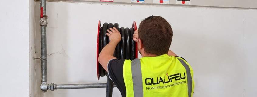 Technicien Qualifeu vérifiant un dévidoir RIA près des panneaux extincteurs et consignes incendie